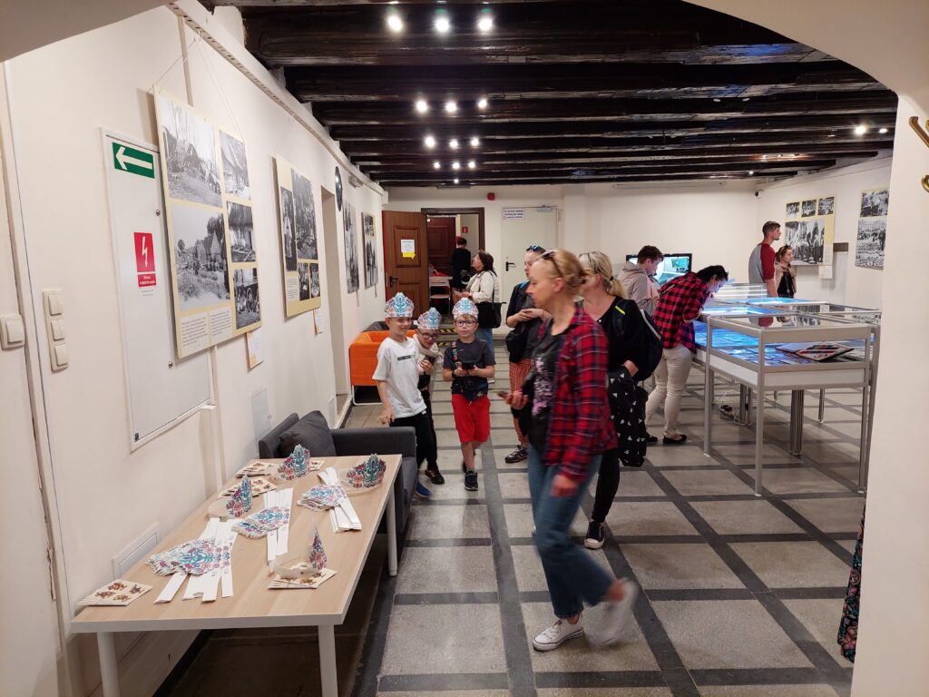 Fotografia zwiedzających oglądających plansze, gabloty i Korony Jagny z papieru.