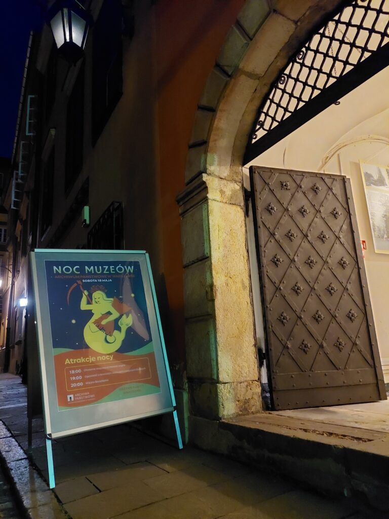 Brama do APW z plakatem Nocy Muzeów 2024 nocą.