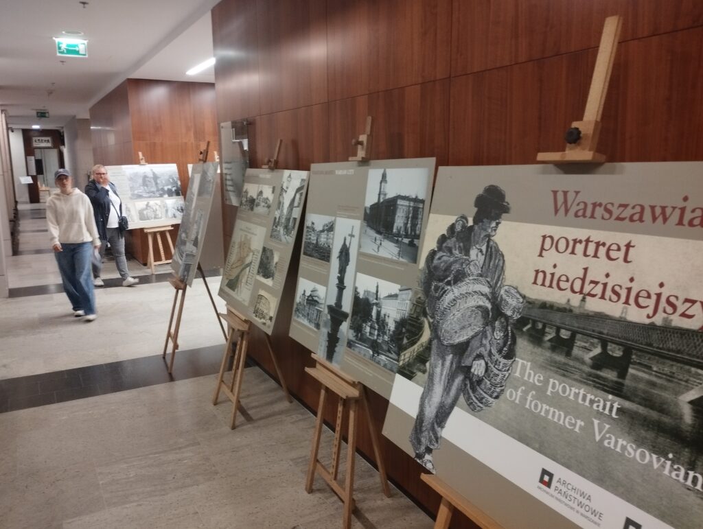 Fragment ekspozycji Warszawiaków portret niedzisiejszy z planszami na sztalugach. Widoczne 3 osoby odwiedzające wystawę.