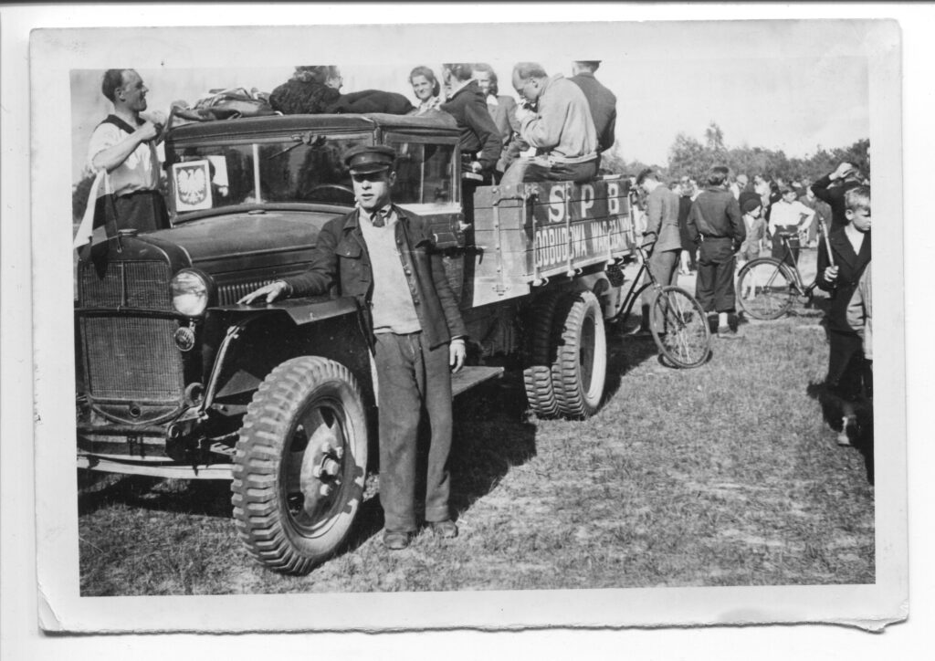 Na czarno-białej fotografii widać grupę ludzi na samochodzie z godłem Polski bez korony i napisem „S.P.B. Odbudowa Warszawy”.