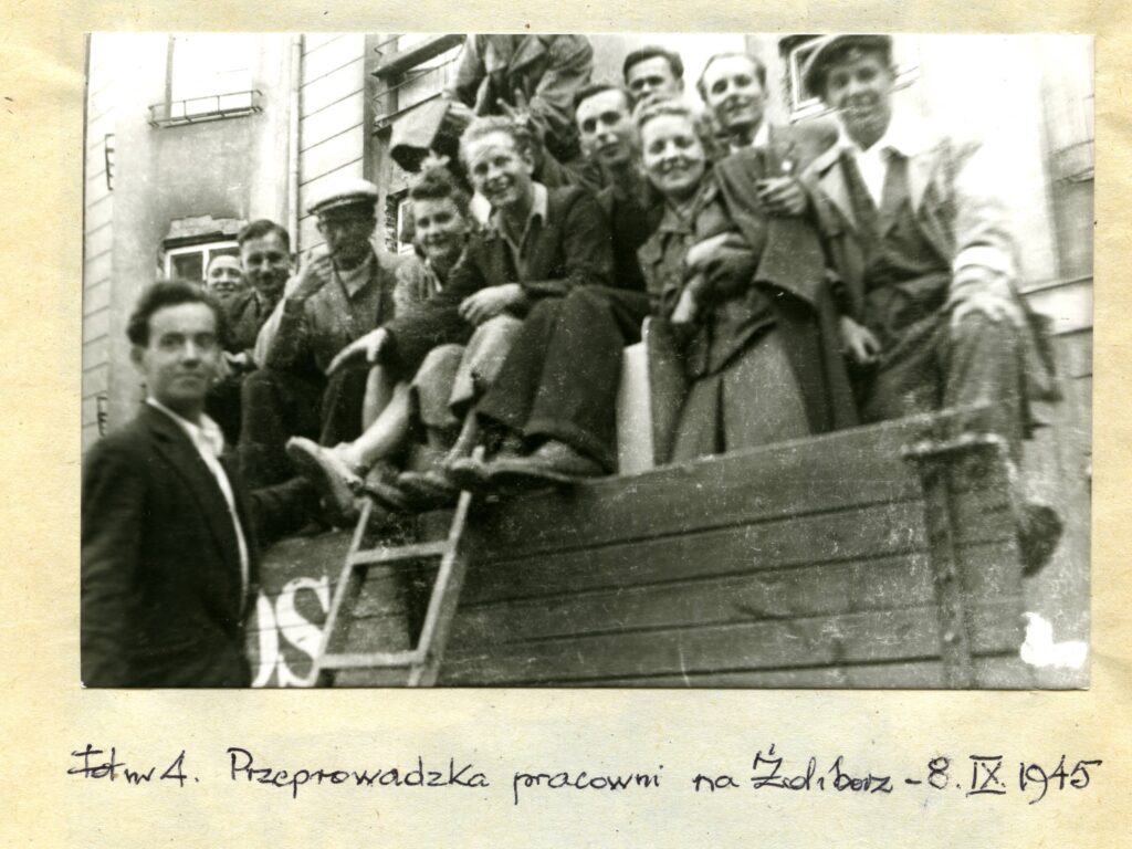 Na czarno-białej fotografii widać grupę młodych ludzi siedzących na pojeździe z napisem „BOS”.