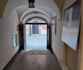 Fotografia kolorowa wyjścia bramy w kamienicy. Na ścianie wisi plansza.