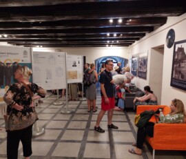 Fotografia kolorowa kilku osób oglądających plansze wystawowe w sali pod modrzewiowym stropem.