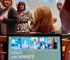 Zdjęcie grupy osób i prezentacji na monitorze komputera (z bliska) i na telebimie (z daleka).