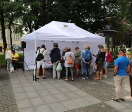 fotografia długiej kolejki osób przed namiotem promocyjnym Archiwów Państwowych. W tle widoczny namiot oraz fragment dibondu wystawy.