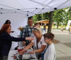 fotografia tłumu odwiedzających stoisko z ulotkami pod namiotem promocyjnym oraz dwóch kobiet z punktu informacyjnego.