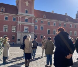 Grupa ludzi na brukowanej ulicy przez Zamkiem Królewskim.