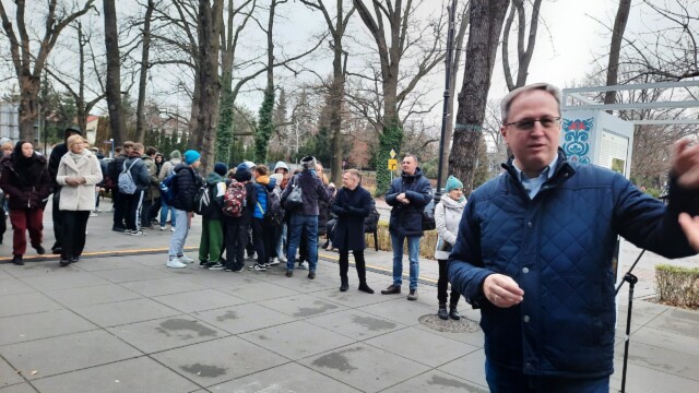 Łukasz Nowacki - specjalista do spraw historii miasta w Ośrodku Kultury Gminy Grodzisk Mazowiecki, fot. M. Goroch Fotografia mężczyzny w niebieskiej kurtce i tłum ludzi w tle.