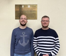 István Balázs - Dyrektor Polskiego Instytutu Badawczego i Muzeum w Budapeszcie, i Adrian Kossowski z Oddziału Popularyzacji Zasobu Archiwalnego APW, fot. A. Szczęsnowicz-Panas Kolorowe zdjęcie dwóch mężczyzn stojących frontem do fotografa. W tle żółta ściana ze złotą tablicą i napisem "Muzeum".