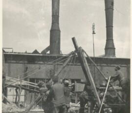 Prace budowalne przy Elektrowni „Powiśle”, 1945 r. Na czarno-białej fotografii widać grupę mężczyzn ustawiających konstrukcję, w tle budynek z dwoma kominami.
