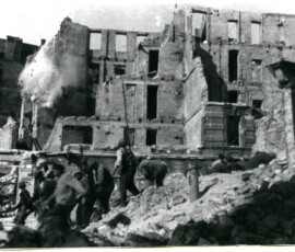 Rozbiórka ruin przy ul. Koszykowej, wrzesień 1945 r. Na czarno-białej fotografii widać grupę ludzi patrzących na wyburzany budynek.
