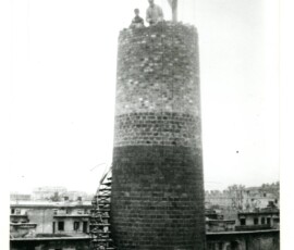 Odbudowa komina kotłowni Warszawskiej Spółdzielni Mieszkaniowej przy ul. Suzina, październik 1945 r. Na czarno-białej fotografii widać wieżę ze schodami budowaną przez dwóch mężczyzn.