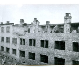 Odbudowa kolonii VIIc Warszawskiej Spółdzielni Mieszkaniowej. Widok od ul. Próchnika, listopad 1945 r. Na czarno-białej fotografii widać grupę ludzi odbudowujących budynek.