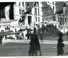 Transparenty z okazji pierwszej rocznicy wyzwolenia Warszawy przy ul. Koszykowej, styczeń 1946 r. Na czarno-białej fotografii widać ruiny budowli, transparent z napisem „Niech żyje bohaterska Warszawa” i spacerujących ludzi.