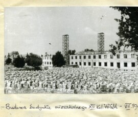 Budowa budynku mieszkalnego XII kolonii Warszawskiej Spółdzielni Mieszkaniowej, lipiec 1947 r. Na czarno-białej fotografii widać wiele cegieł i odbudowywany budynek w tle z dwoma masztami.