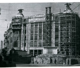 Gmach Banku Gospodarstwa Spółdzielczego (dom „Pod Orłami”) przy ul. Jasnej 1, wrzesień 1947 r. Na czarno-białej fotografii widać odbudowywany budynek zwieńczony dwoma orłami i tablicę z napisem informującym o budowie.