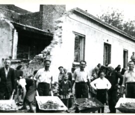 Prace rozbiórkowe na terenie Ośrodka Zdrowia przy ul. Słowackiego 45, wrzesień 1947 r. Na czarno-białej fotografii widać czterech mężczyzn z taczkami, w tle grupa ludzi i zrujnowany budynek.