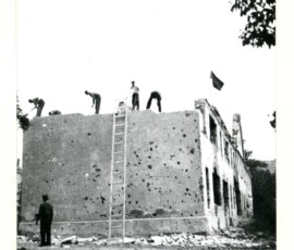 Rozbiórka budynku mieszkalnego przy ul. Harcerskiej 2 (ob. al. Harcerska), wrzesień 1947 r. Na czarno-białej fotografii widać grupę mężczyzn odbudowujących budynek zwieńczony flagą, a przy nim drabinę.