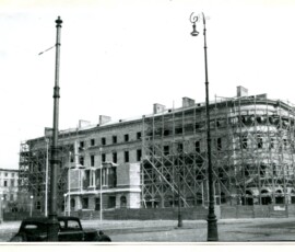 Odbudowa budynków wojskowych na placu Zwycięstwa (ob. plac Piłsudskiego), luty 1948 r. Na czarno-białej fotografii widać odbudowywany budynek, a na pierwszym planie jadący samochód i dwie latarnie.