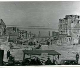 Rejon ul. Senatorskiej i ul. Miodowej, kwiecień 1948 r. Na czarno-białej fotografii widać mężczyznę w pojeździe oznaczonym „Beton-Stal”, w tle grupa mężczyzn, sprzęt budowlany i ruiny budynków.