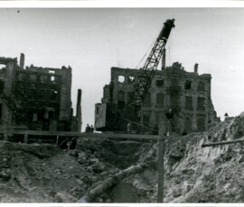 Budowa tunelu pod Krakowskim Przedmieściem, kwiecień 1948 r. Na czarno-białej fotografii widać rozkopaną ziemię, w tle sprzęt budowlany, grupa ludzi i ruiny budynków.