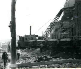 Kolejka wywożąca gruz na Krakowskim Przedmieściu, kwiecień 1948 r. Na czarno-białej fotografii widać grupę robotników, sprzęt budowlany i budynki w tle.