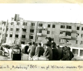 „Autobusy” Biura Odbudowy Stolicy na pl. Wilsona, wrzesień 1945 r. Na czarno-białej fotografii widać grupę ludzi siedzących na pojeździe z napisem „BOS”, w tle zniszczony budynek.