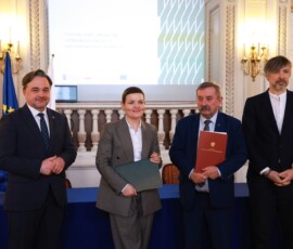 Fotografia kolorowa. Dwóch mężczyzn stoi. Kobieta i mężczyzna stoją z teczkami w rękach.