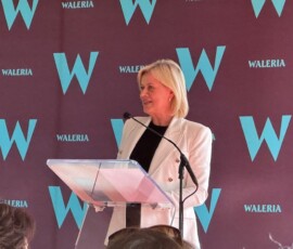 Wiceminister Bożena Żelazowska, sekretarz stanu w Ministerstwie Kultury i Dziedzictwa Narodowego, fot. M. Wiercińska Fotografia kolorowa kobiety w blond włosach, stojącej na mównicy z mikrofonem. W tle bordowa plansza z błękitnymi literami.