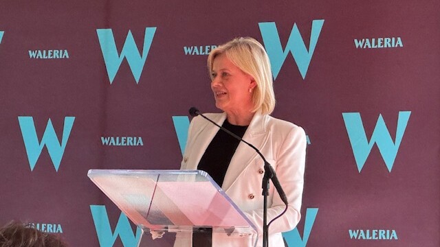 Wiceminister Bożena Żelazowska, sekretarz stanu w Ministerstwie Kultury i Dziedzictwa Narodowego, fot. M. Wiercińska Fotografia kolorowa kobiety w blond włosach, stojącej na mównicy z mikrofonem. W tle bordowa plansza z błękitnymi literami.