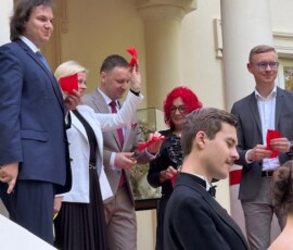 Wiceminister Bożena Żelazowska, Jan Krześniak, Artur Niedziński, Ewa Mickiewicz i Marcin Dawidowicz, fot. M. Wiercińska Fotografia kobiet i mężczyzn z czerwonymi chusteczkami, stojących przed wejściem do budynku z kolumnami.