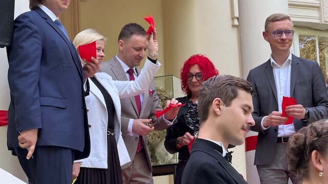 Wiceminister Bożena Żelazowska, Jan Krześniak, Artur Niedziński, Ewa Mickiewicz i Marcin Dawidowicz, fot. M. Wiercińska Fotografia kobiet i mężczyzn z czerwonymi chusteczkami, stojących przed wejściem do budynku z kolumnami.