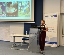 Archiwista Irena Mackiewicz z Archiwum Państwowego w Warszawie Oddziału w Otwocku na IX Ogólnopolskiej Konferencji Archiwistów i Historyków z cyklu „Educare necesse est…”. Na kolorowej fotografii widać kobietę przy mikrofonie przed pulpitem, w tle prezentacja i baner z logotypem Mazowieckiego Samorządowego Centrum Doskonalenia Nauczycieli.