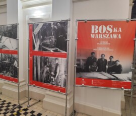 Wystawa „BOS-ka Warszawa. Herosi odbudowy” w Gmachu Głównym Politechniki Warszawskiej. Na kolorowej fotografii widać plansze wystawiennicze, w tle ściana i schody.