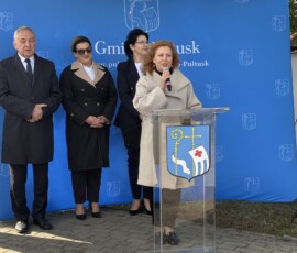 Przemawia Dyrektor Archiwum Państwowego w Warszawie Magdalena Wiercińska Na zdjęciu widać kobietę z mikrofonem przy pulpicie, w tle dwie kobiety i mężczyzna oraz baner z napisem Gmina Pułtusk i herbem miasta.