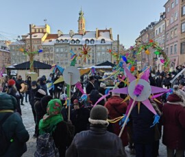 Staromiejskie Kolędowanie na Rynku Starego Miasta
Fot. A. Smyk Na kolorowym zdjęciu widać tłum ludzi w czapkach i kurtkach, z których cztery osoby trzymają papierowe gwiazdy, w tle widać kamienice ze śniegiem na dachach.